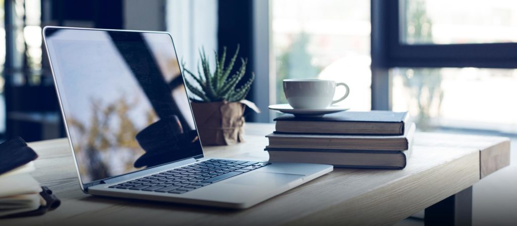 Laptop steht auf einem Tisch daneben eine Tasse auf einem Stapel Bücher