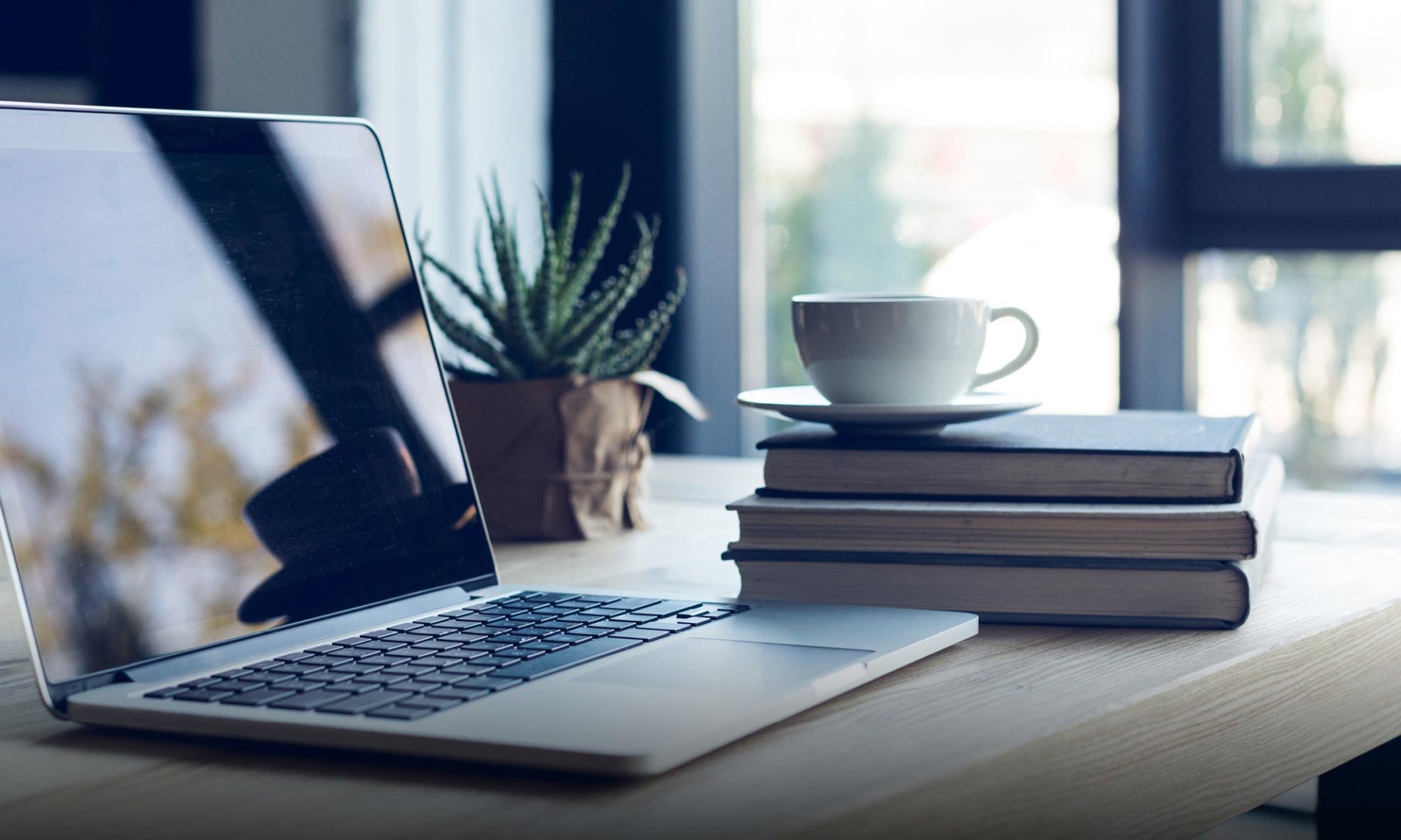 Laptop steht auf einem Tisch daneben eine Tasse auf einem Stapel Bücher