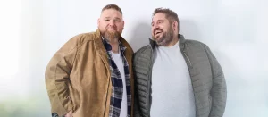 Zwei Männer mit Übergröße: links in Lederjacke mit offenem Karohemd und weißem T-Shirt, rechts in grüner Steppjacke mit grauem Pullover