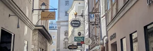 Historische Gasse in Salzburg mit kunstvollen Wirtshausschildern bekannter Gastronomiebetriebe, darunter das Augustiner Bräu.