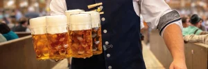 Männlicher Kellner in Tracht trägt fünf Maß Bier durch das Festzelt auf einem Volksfest.