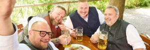Vier Männer in traditioneller Tracht sitzen zusammen auf einem bayerischen Fest und trinken eine Maß Bier.