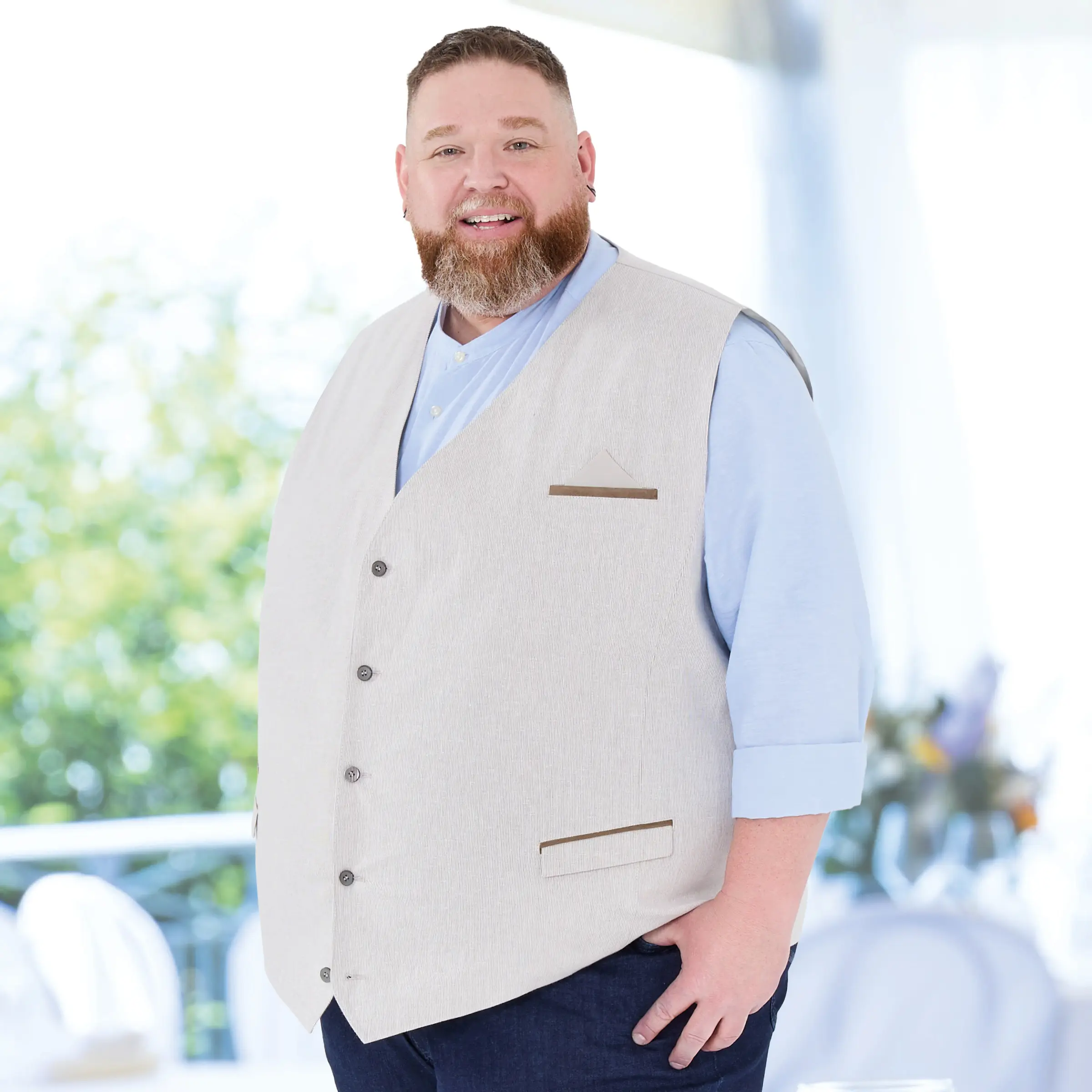 Ein selbstbewusster Mann in großer Größe trägt eine elegante, sommerliche Weste mit hellblauem Hemd und dunkler Jeans. Perfekt für Gartenfeste, Hochzeiten oder entspannte Feierlichkeiten – Mode, die passt und Persönlichkeit zeigt.
