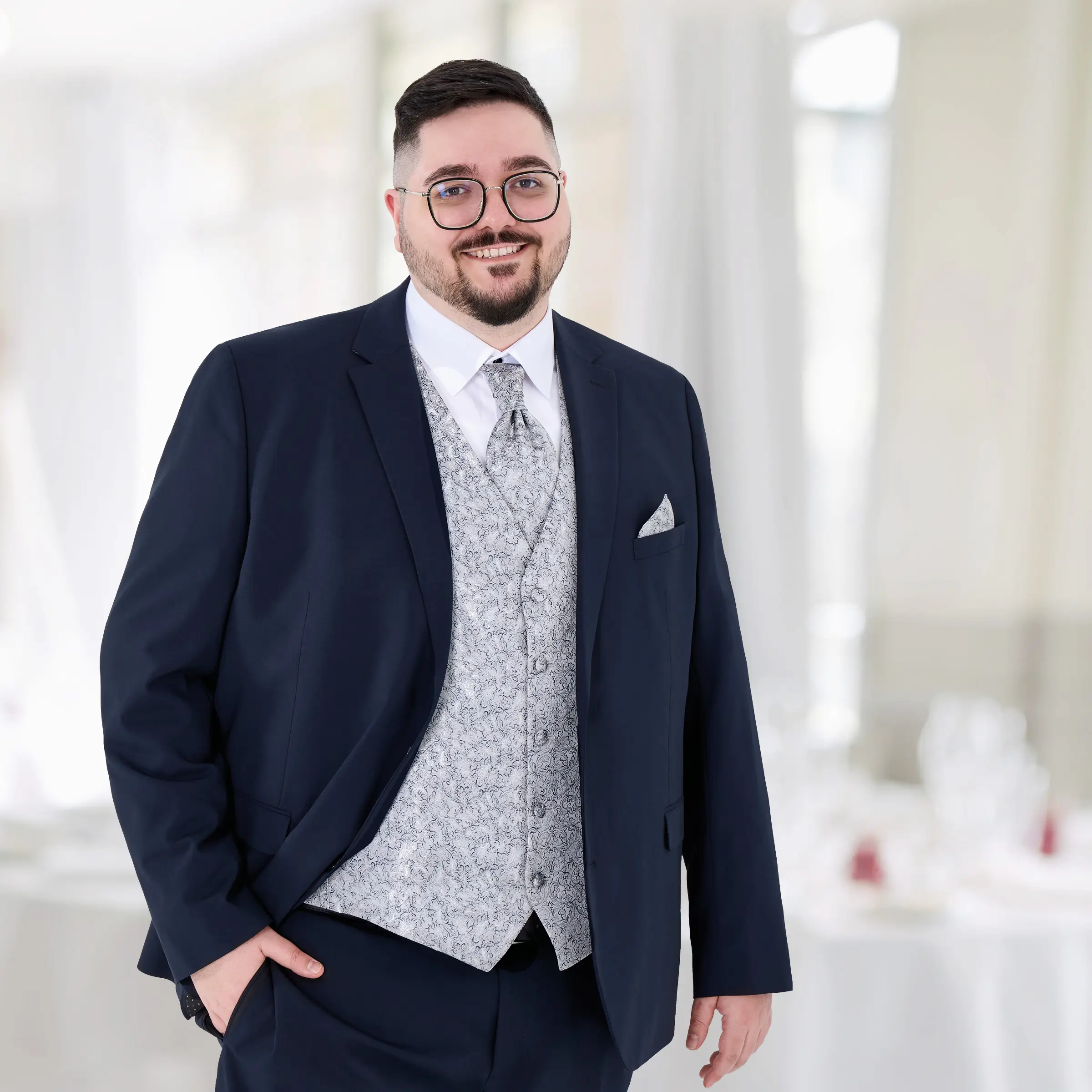 Ein stilvoller Mann mit Format trägt einen dunkelblauen Anzug mit silbergrauer Schmuckweste und passender Krawatte. Der Look ist ideal für Hochzeiten, Empfänge oder festliche Events – selbstbewusst, gepflegt und perfekt auf große Größen abgestimmt.