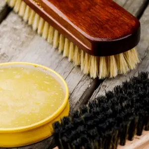 Nahaufnahme von Lederfett und verschiedenen Pflegebürsten auf Holz