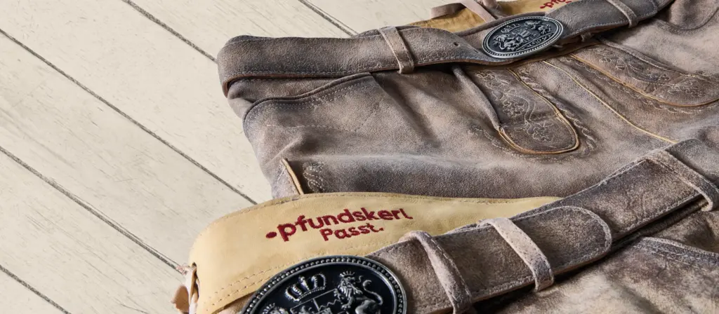 Zwei helle Lederhosen mit besticktem „Pfundskerl Passt“-Bund