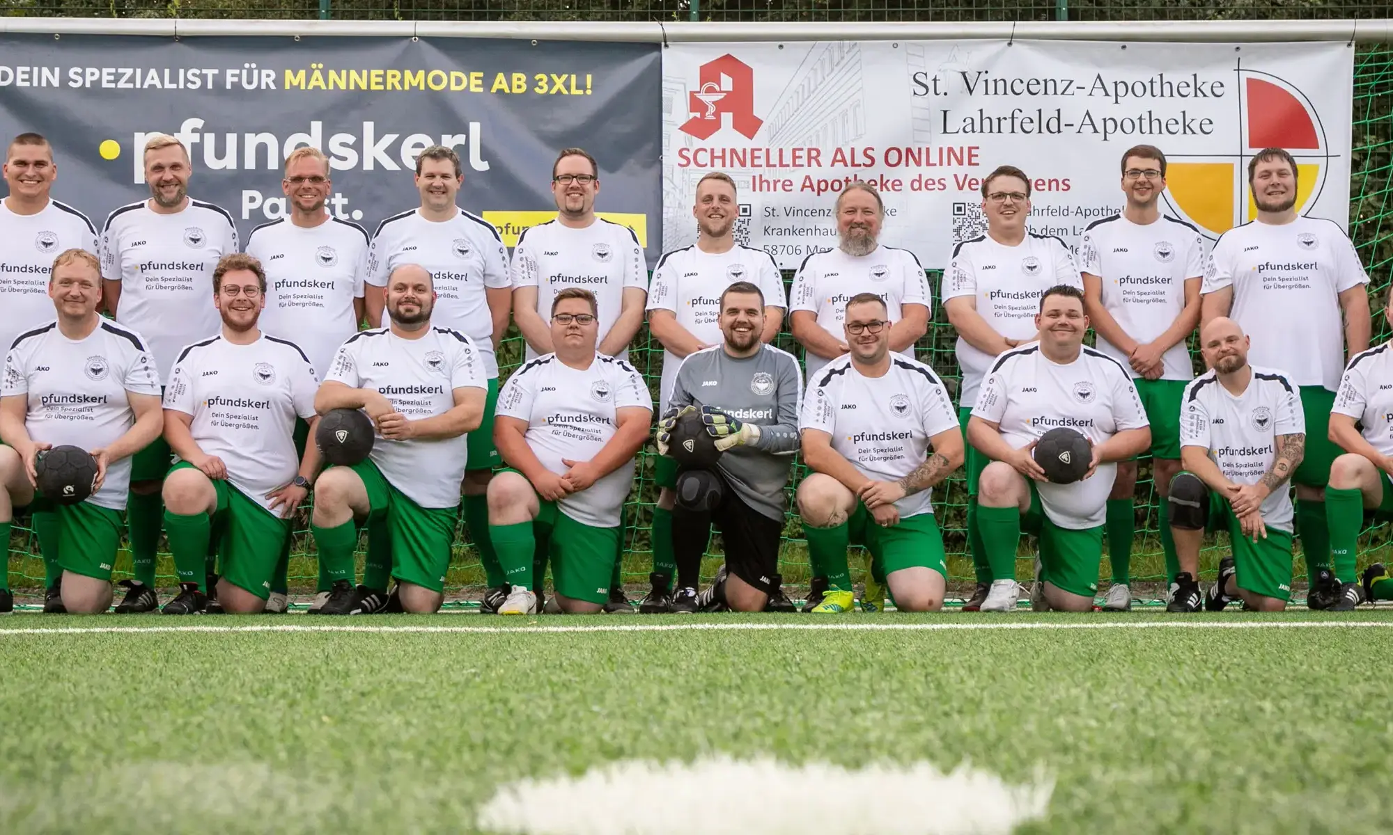 Mannschaftsfoto der Mendener Pfundskerle in weißen Trikots vor Sponsorwand