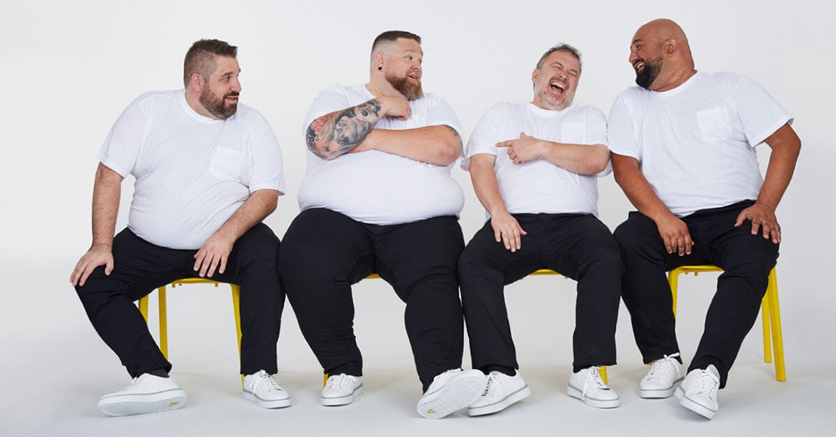 Vier Männer in großen Größen sitzen lachend nebeneinander – authentische Herrenmode bei Pfundskerl.