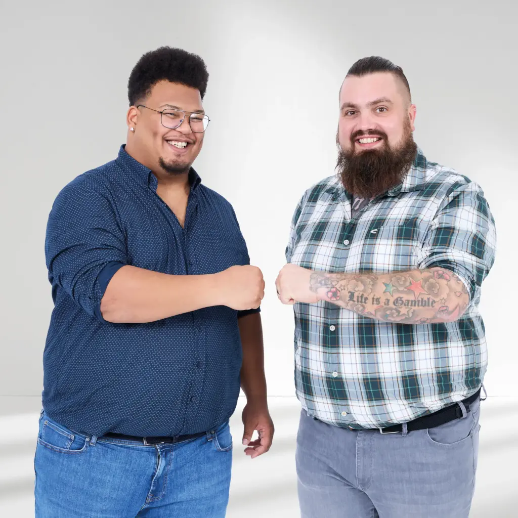 Zwei kräftige Männer in Freizeitmode grüßen sich mit Faustcheck – Plus Size Mode mit Charakter und Echtheit.