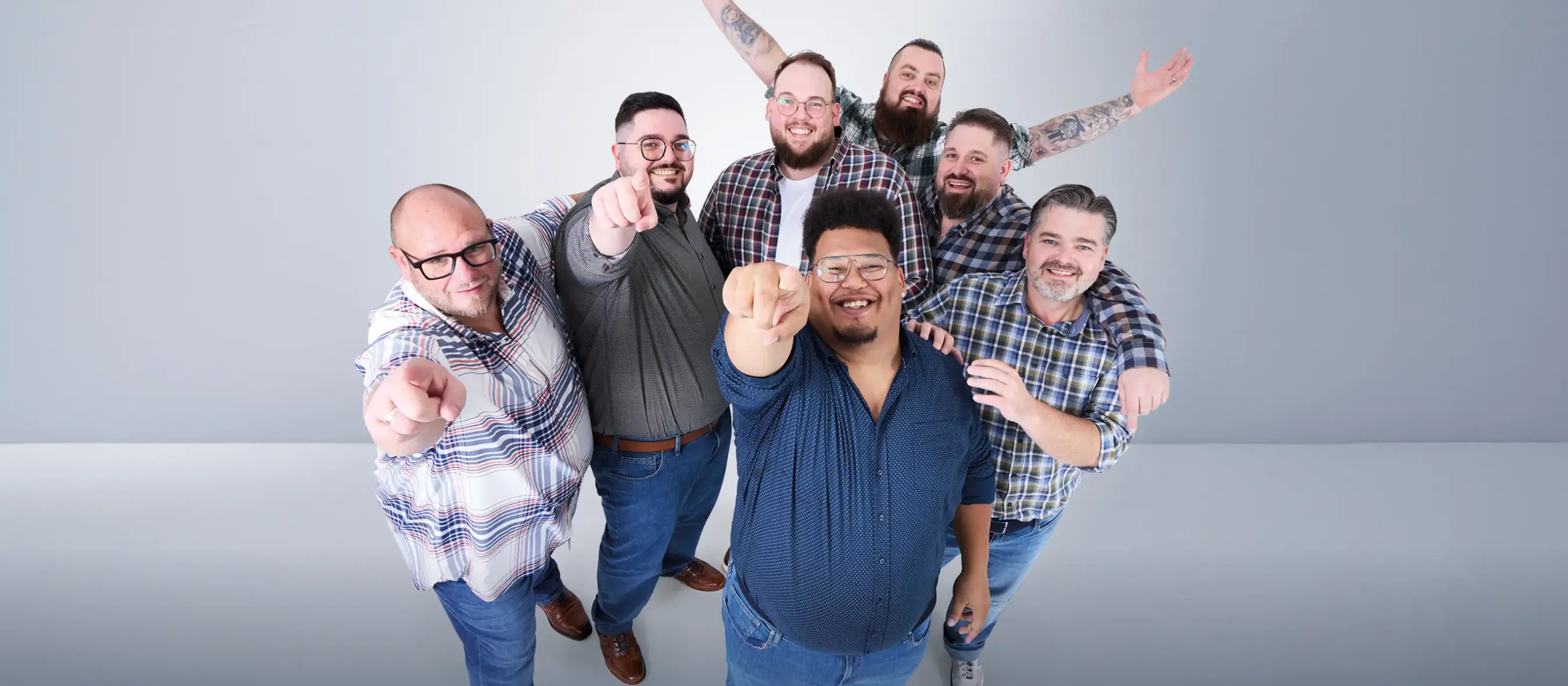 Gruppe echter Pfundskerl-Models zeigt lachend auf die Kamera