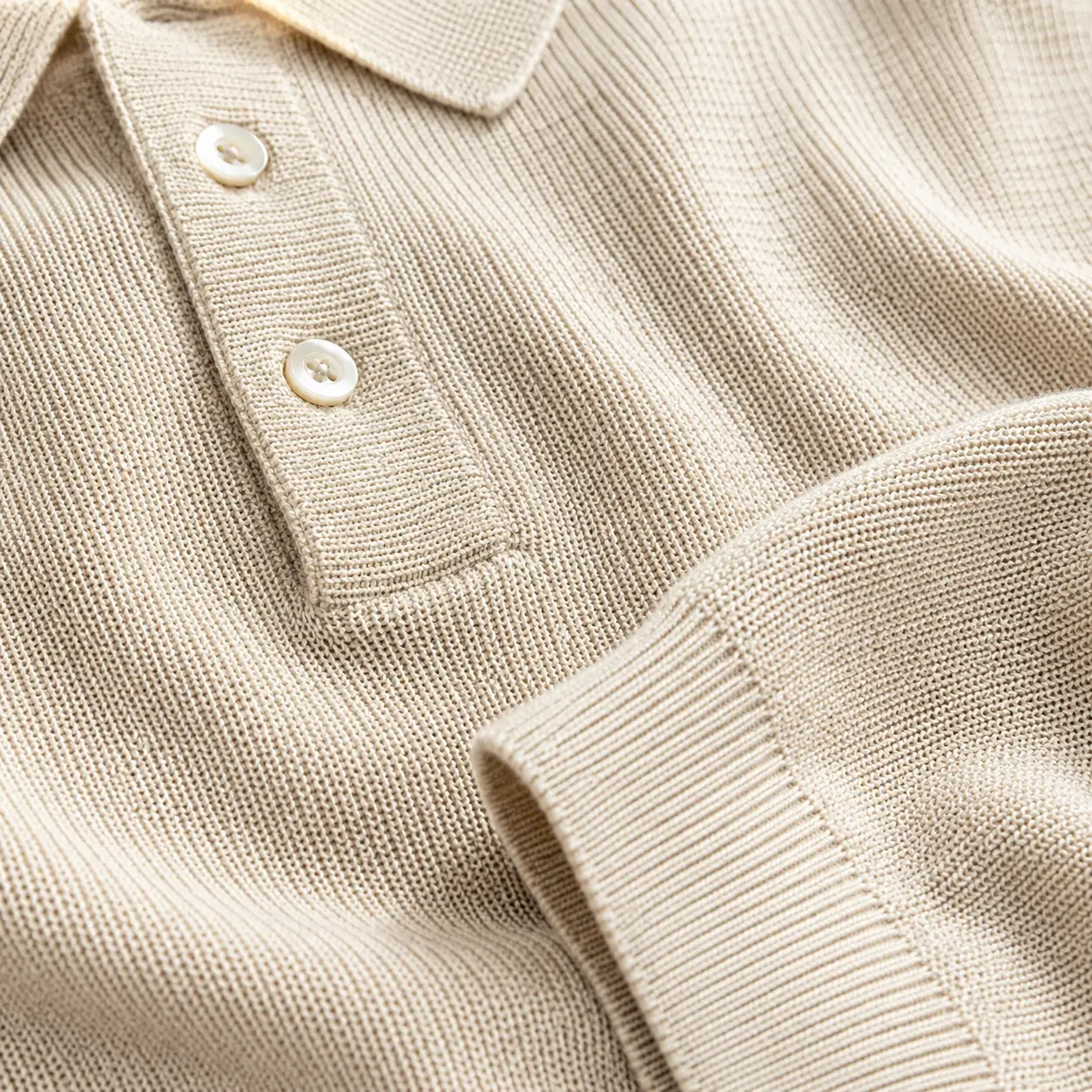 Detailaufnahme eines beigen Strickpoloshirts mit feiner Strickstruktur, Polokragen und Knopfleiste.