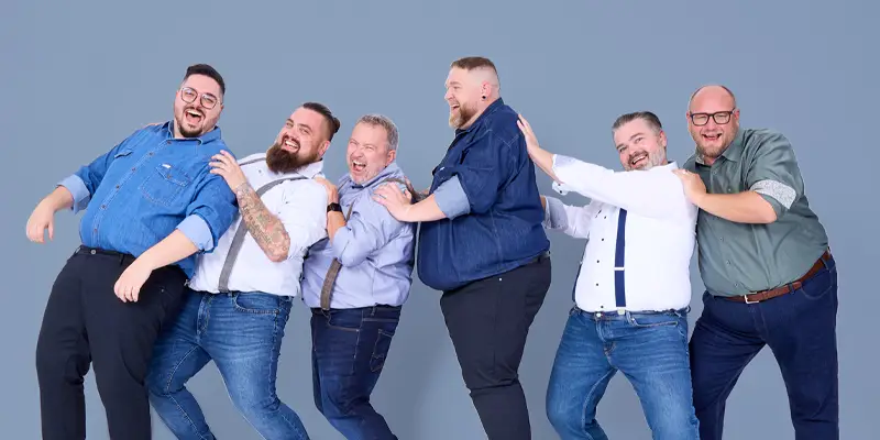 Sechs Männer in großen Größen lachen und stehen in dynamischer Pose – unser starkes Team