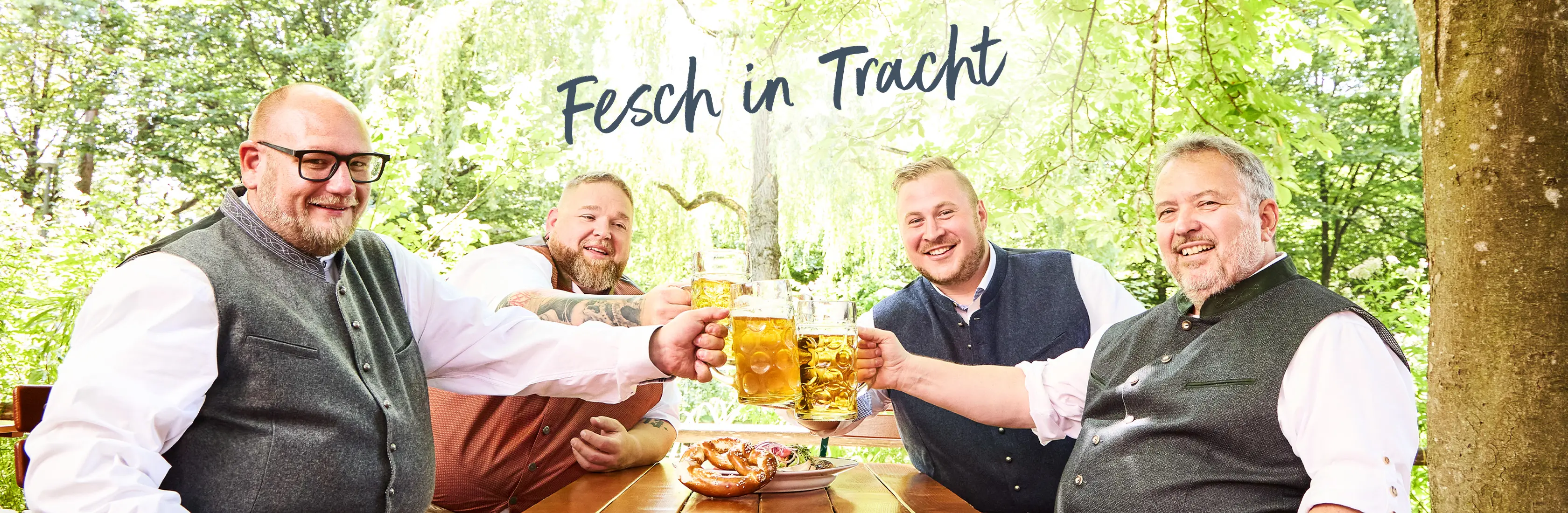 Zwei Männer in grauen Trachtenwesten, weißen Hemden und Lederhosen im Biergarten – traditioneller Stil für Männer mit Bauch und Charakter.