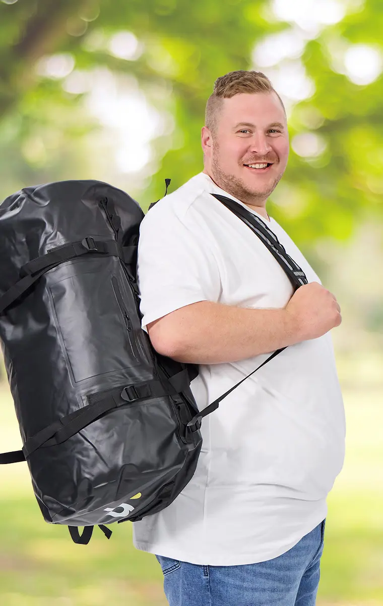 Kräftiger Mann mit XXL-T-Shirt und riesigem schwarzen Rucksack in Naturkulisse