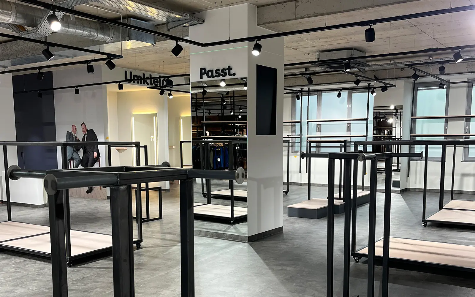 Leerer Verkaufsraum mit Kleiderstangen und Umkleidekabinen im Bau – moderner Storeumbau bei Pfundskerl mit neuen Spiegeln, Lichtelementen und Fototapete im Hintergrund