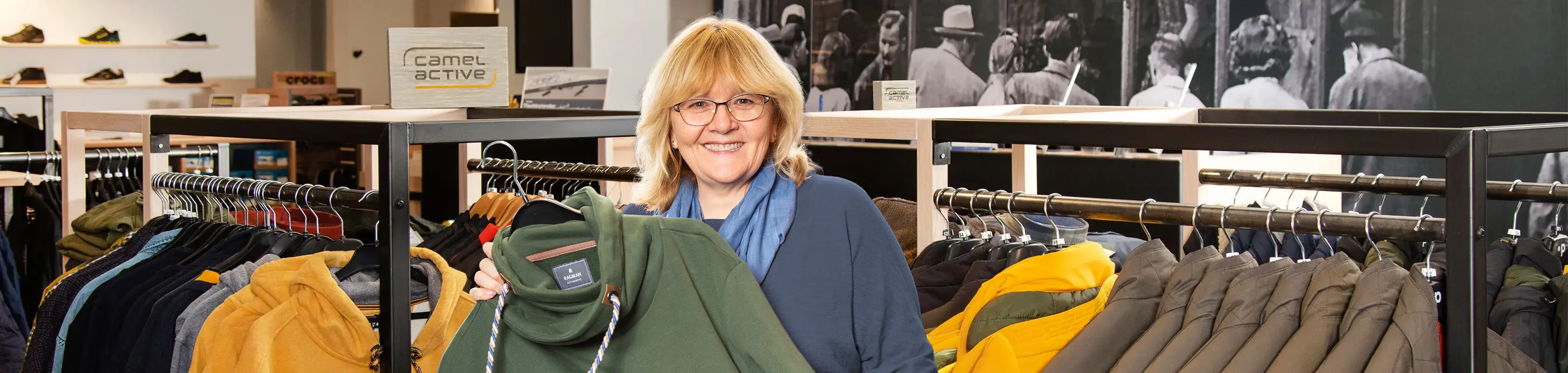 Pfundskerl-Mitarbeiterin berät Kunden im Store und zeigt ein grünes Sweatshirt