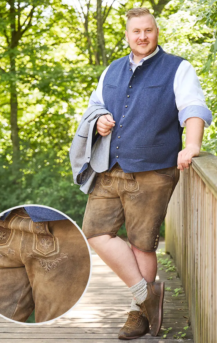 Großer Mann in Tracht mit blauer Weste, weißem Hemd und bestickter Lederhose