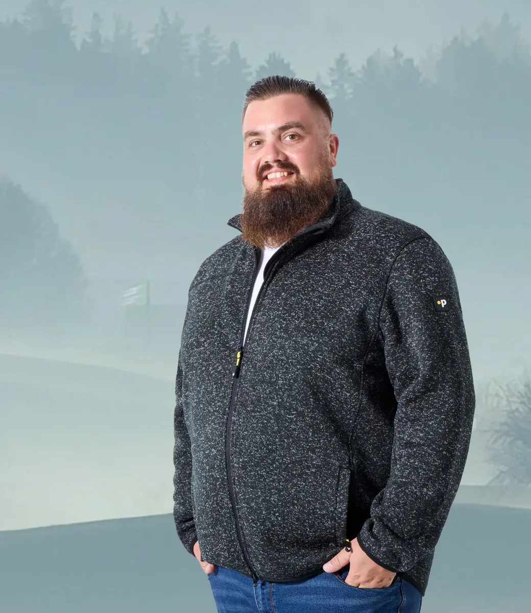 Mann mit grauer Fleecejacke in großer Größe vor Outdoor-Kulisse