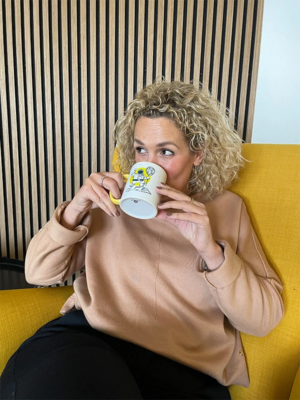 Frau mit lockigem Haar trinkt aus dem Pfundskerl-Sammeltassenbecher mit Astronautenmotiv