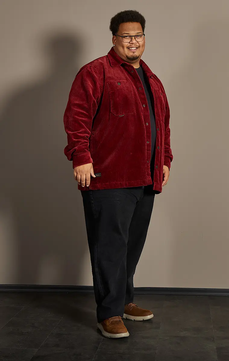 Mann in großer Größe mit roter Cordjacke und schwarzem Shirt vor neutralem Hintergrund