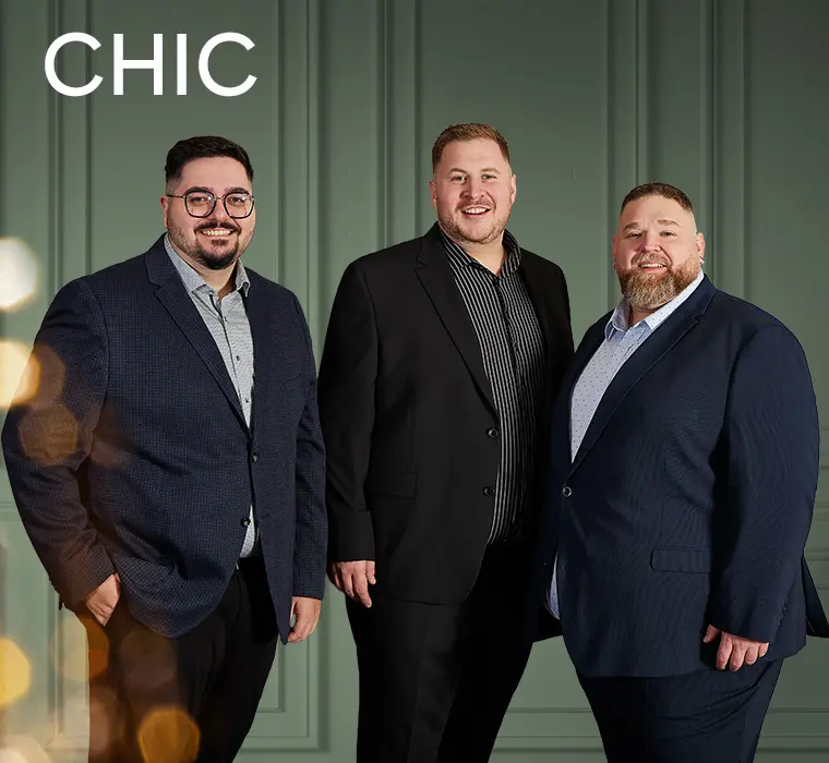 Drei Männer in eleganten Anzügen und Hemden vor dunkelblauem Hintergrund.