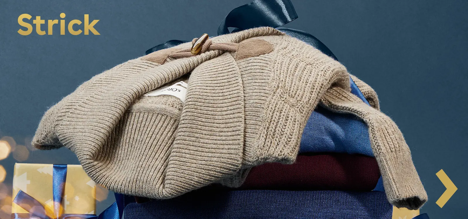 Weiche Strickteile und Pullover in Naturtönen liebevoll gestapelt und mit blauer Schleife dekoriert.