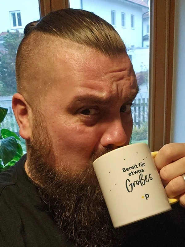 Pfundskerl-Kunde trinkt ernst blickend aus der Sammel-Tasse mit der Aufschrift „Bereit für etwas Großes“