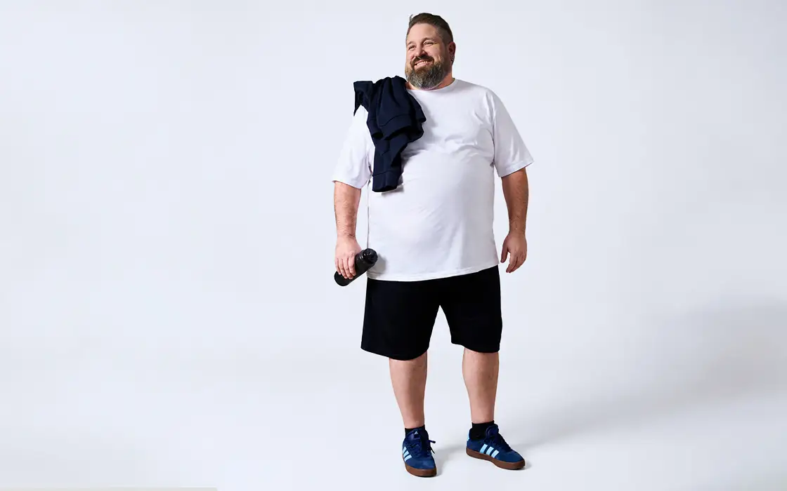 Starker Mann im weißen T-Shirt und schwarzen Shorts mit Trinkflasche als Sportlook in großen Größen