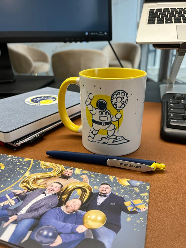 Pfundskerl-Sammeltasse mit Astronautenmotiv auf Schreibtisch neben Grußkarte und Kugelschreiber