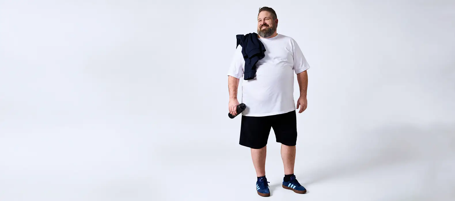 Starker Mann im weißen T-Shirt und schwarzen Shorts mit Trinkflasche als Sportlook in großen Größen