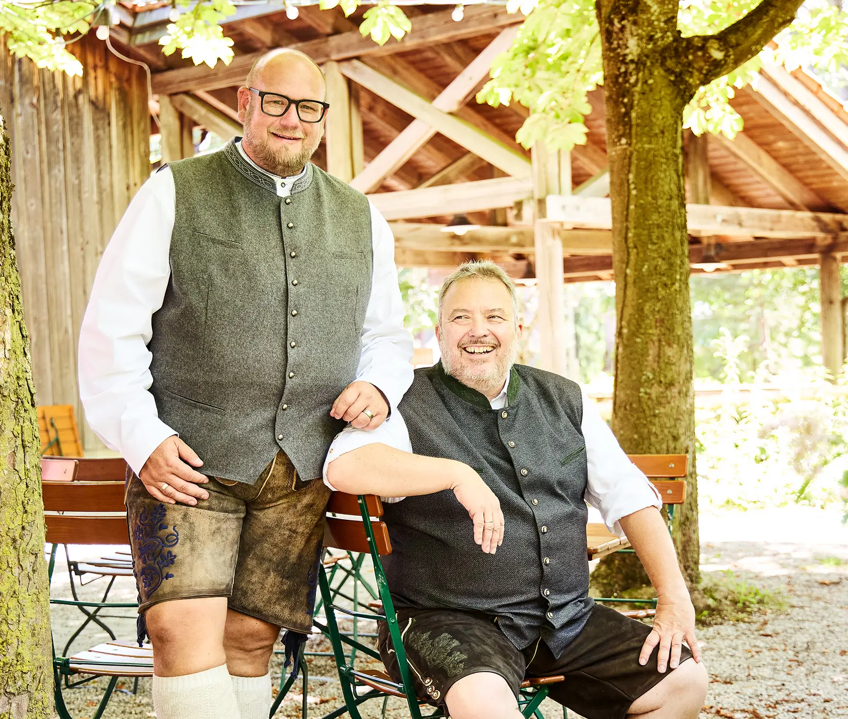 Zwei Männer mit kräftiger Statur in klassischer Trachtenweste und rustikaler Lederhose – bequeme Passform für den XXL-Biergartenbesuch.