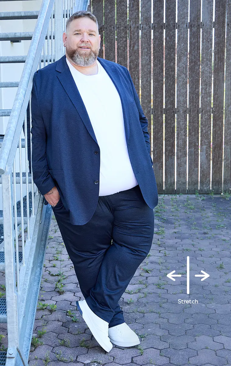 Großer Mann in XXL-Anzug mit weißem Shirt und weißen Sneakern an einer Metalltreppe