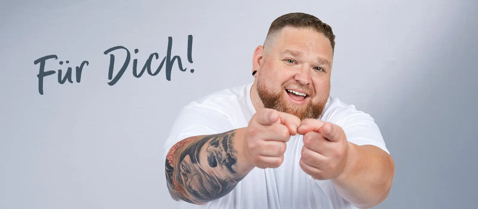Lächelnder Mann im weißen Shirt zeigt auf den Betrachter vor dem „Für Dich!“-Schriftzug