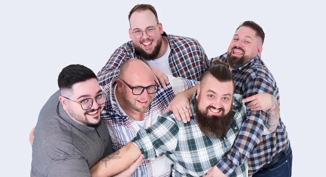Fünf gut gelaunte Männer in lässigen Hemden stehen gemeinsam vor hellem Hintergrund und lachen in die Kamera.