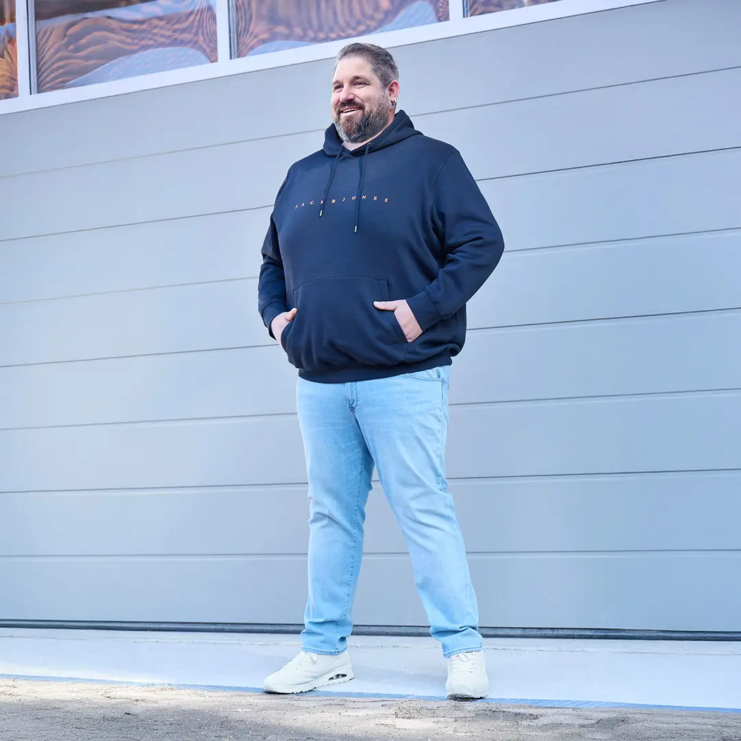 Mann in dunkelblauem Hoodie mit Logo und hellblauer Jeans – sportiver Freizeitlook mit Wohlfühlfaktor.