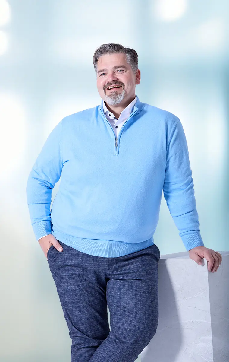 Mann im hellblauen Pullover mit Hemd und karierter Hose – stilvoller Businesslook in großen Größen