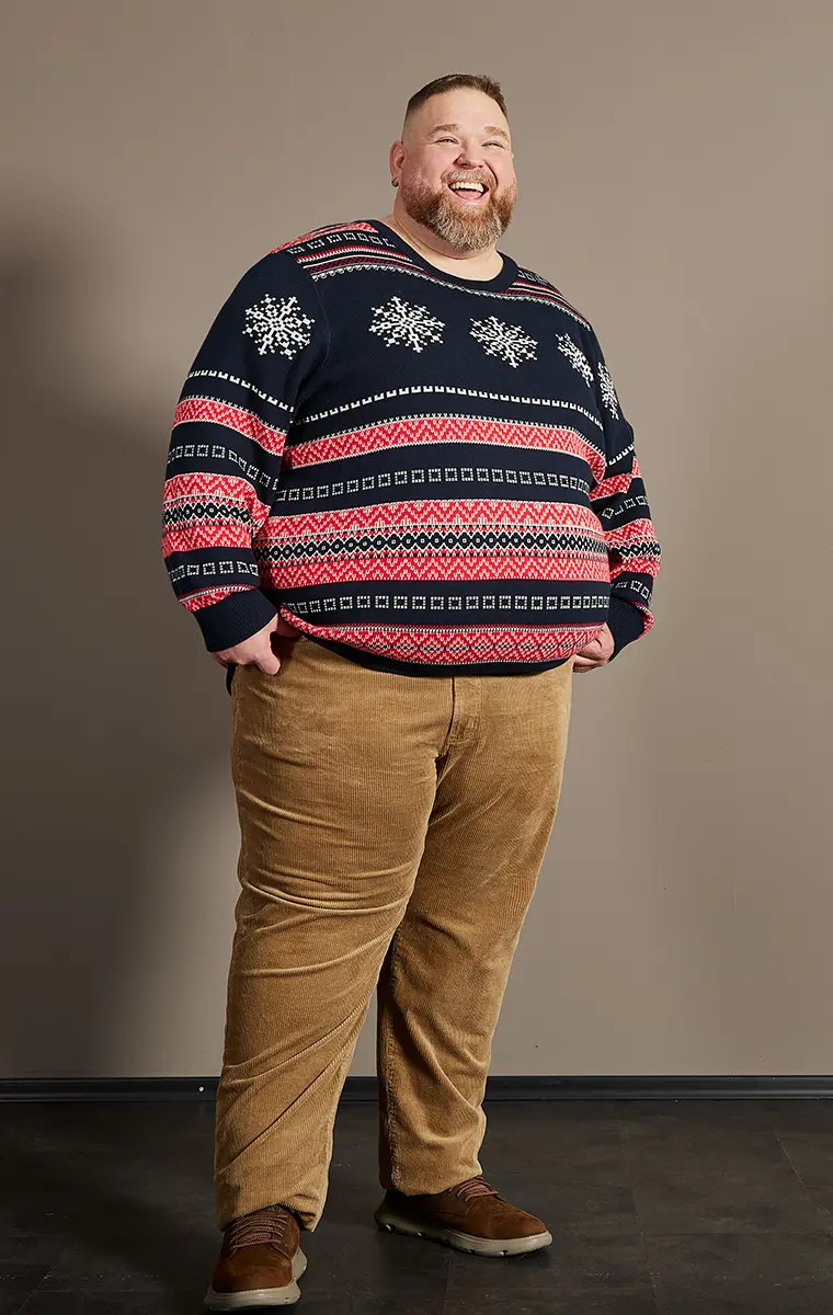 Mann in großer Größe mit Norwegerpullover und Cordhose im Studio