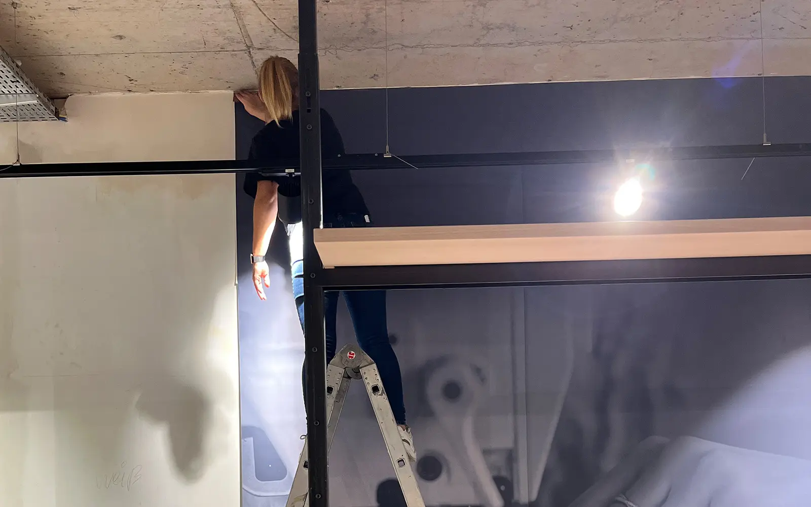 Frau auf Leiter bringt großformatige Fototapete an die Wand im neuen Pfundskerl-Store an – ein Blick hinter die Kulissen des Umbaus