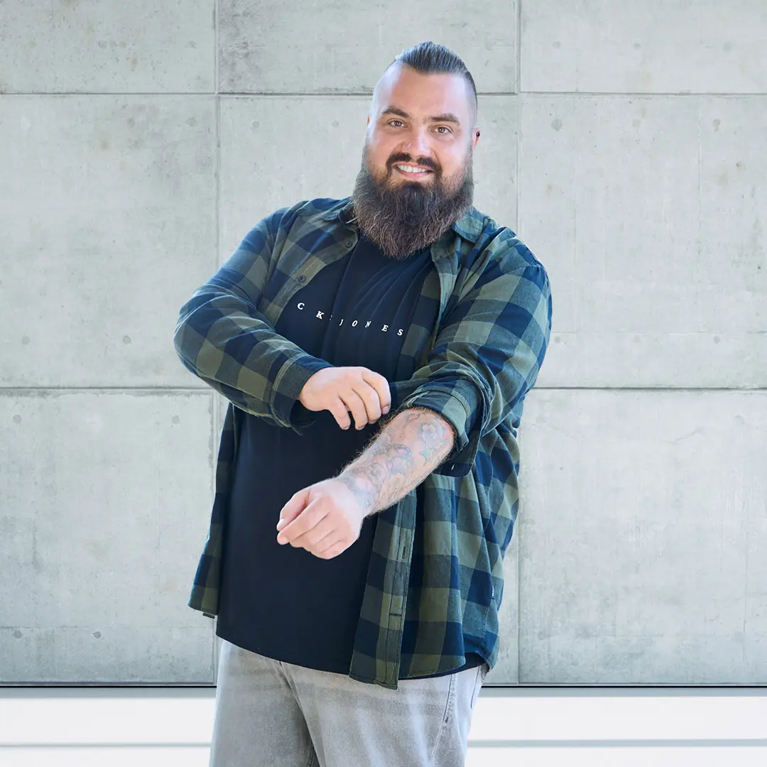 Mann mit Vollbart in schwarzem Jack & Jones T-Shirt und offenem grün-schwarzen Karohemd – stylisches Outfit in großen Größen.