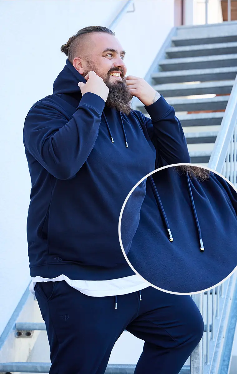 Großer Mann im Hoodie zieht Kapuze auf, Detailansicht zeigt hochwertige Metallkordelenden