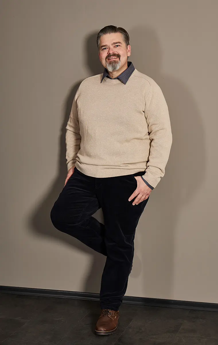 Mann in großer Größe mit beigem Pullover und dunkler Cordhose im Studio