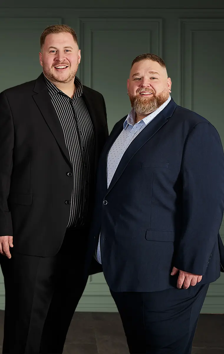 Zwei Männer in großen Größen tragen festliche Anzüge in Schwarz und Dunkelblau als elegante Weihnachtsoutfits