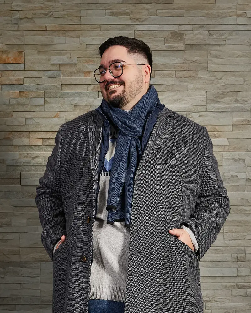 Mann im eleganten Mantel mit Schal in XXL vor einer Steinwand – warmer, stilvoller Winterlook für starke Männer