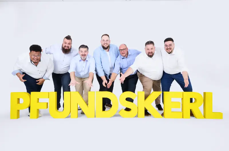 Sieben Männer stehen gut gelaunt hinter großen gelben Pfundskerl Buchstaben vor einem hellen Hintergrund.