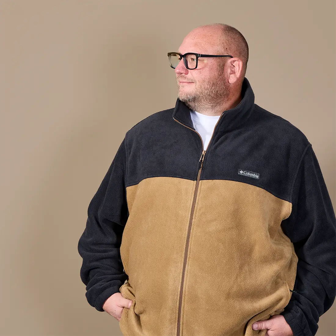 Mann in großer Größe trägt eine zweifarbige Fleecejacke in Schwarz und Beige mit Reißverschluss und Stehkragen.