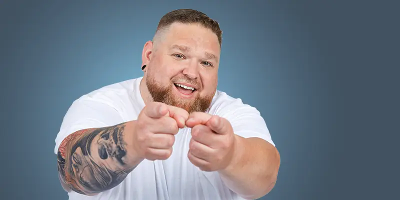 Pfundskerl mit Tattoos zeigt mit beiden Fingern auf die Kamera – Werde ein Pfundskerl Experte
