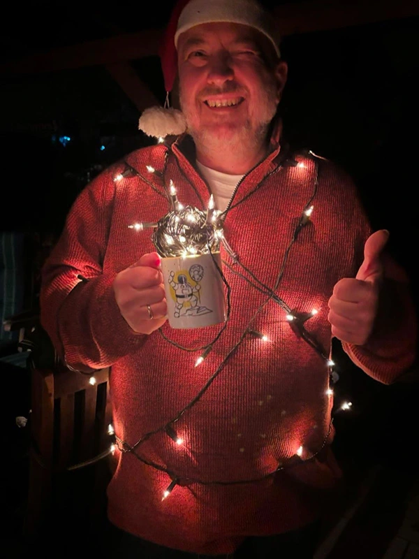 Mann mit Nikolausmütze und Lichterkette hält lächelnd die Pfundskerl-Sammeltasse mit Astronaut in der Hand