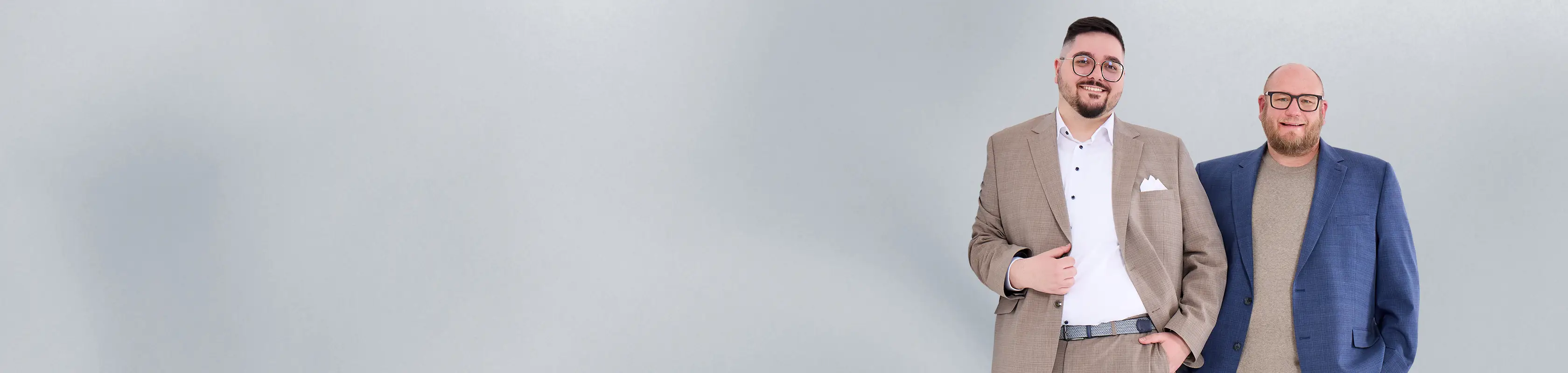 Zwei kräftige Männer in eleganten Sakkos vor grauem Hintergrund – selbstbewusst, stilsicher und perfekt gekleidet in großen Größen