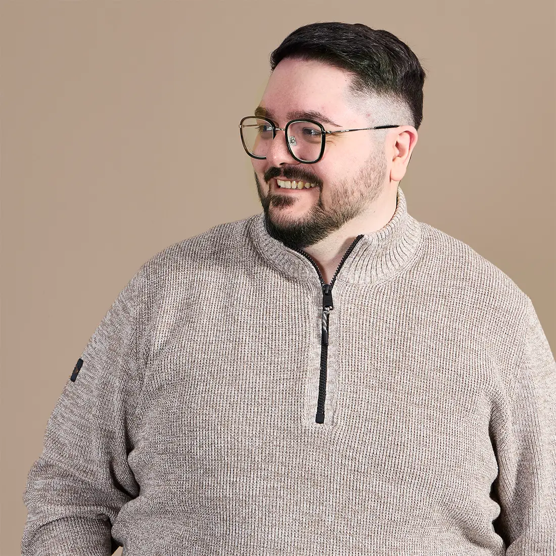 Mann in großer Größe trägt einen beigen Strickpullover mit Stehkragen und kurzem Reißverschluss.