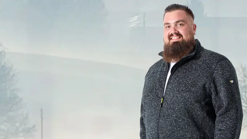 Mann mit grauer Fleecejacke in großer Größe vor Outdoor-Kulisse